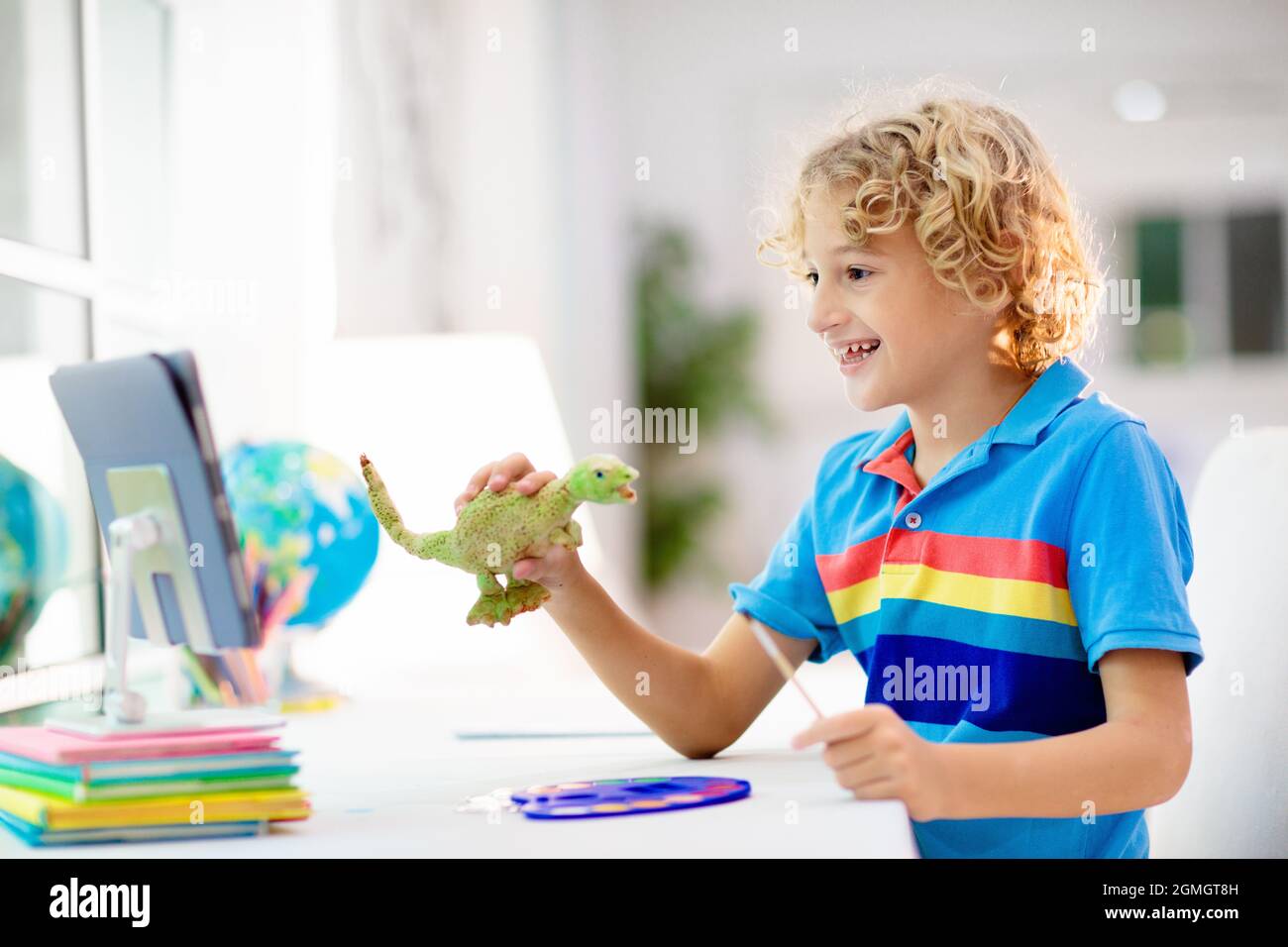 Online-Fernunterricht. Schulkinder mit Computer, die mit dem Lehrer und der Klassengruppe über Videokonferenzen chatten. Kind Färbung Ton Dinosaurier. Stockfoto