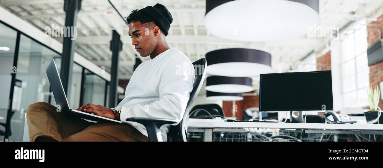 Computerprogrammierer, der in einem Büro an einem neuen Code arbeitet. Fokussierter junger Geschäftsmann mit einem Laptop an einem modernen Arbeitsplatz. Kreative Geschäftsleute Stockfoto