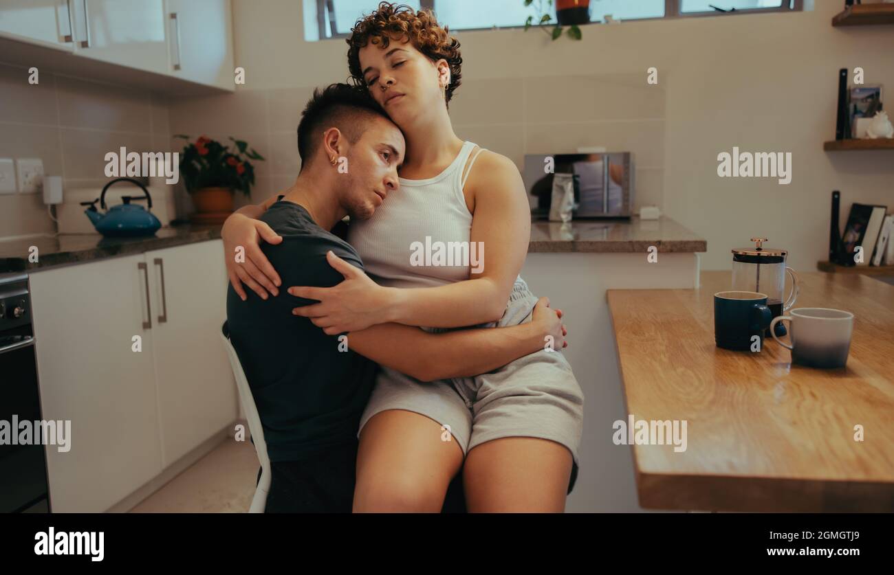 Junge Frau, die sich zu Hause mit ihrem Freund verklebt. Anhänglich junge Frau umarmt ihren Freund, während sie auf seinem Schoß sitzt. Romantisches junges queeres Paar Stockfoto