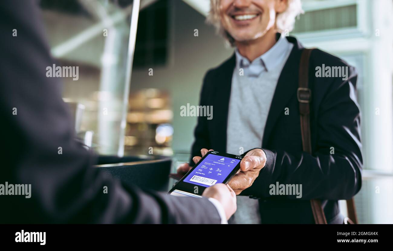 Ausschnittene Aufnahme eines männlichen Passagiers, der mit einem digitalen Flugticket am Flughafenterminal eingecheckt hat. Geschäftsmann zeigt den Mitarbeitern die Bordkarte des Flugzeugs auf dem Handy Stockfoto