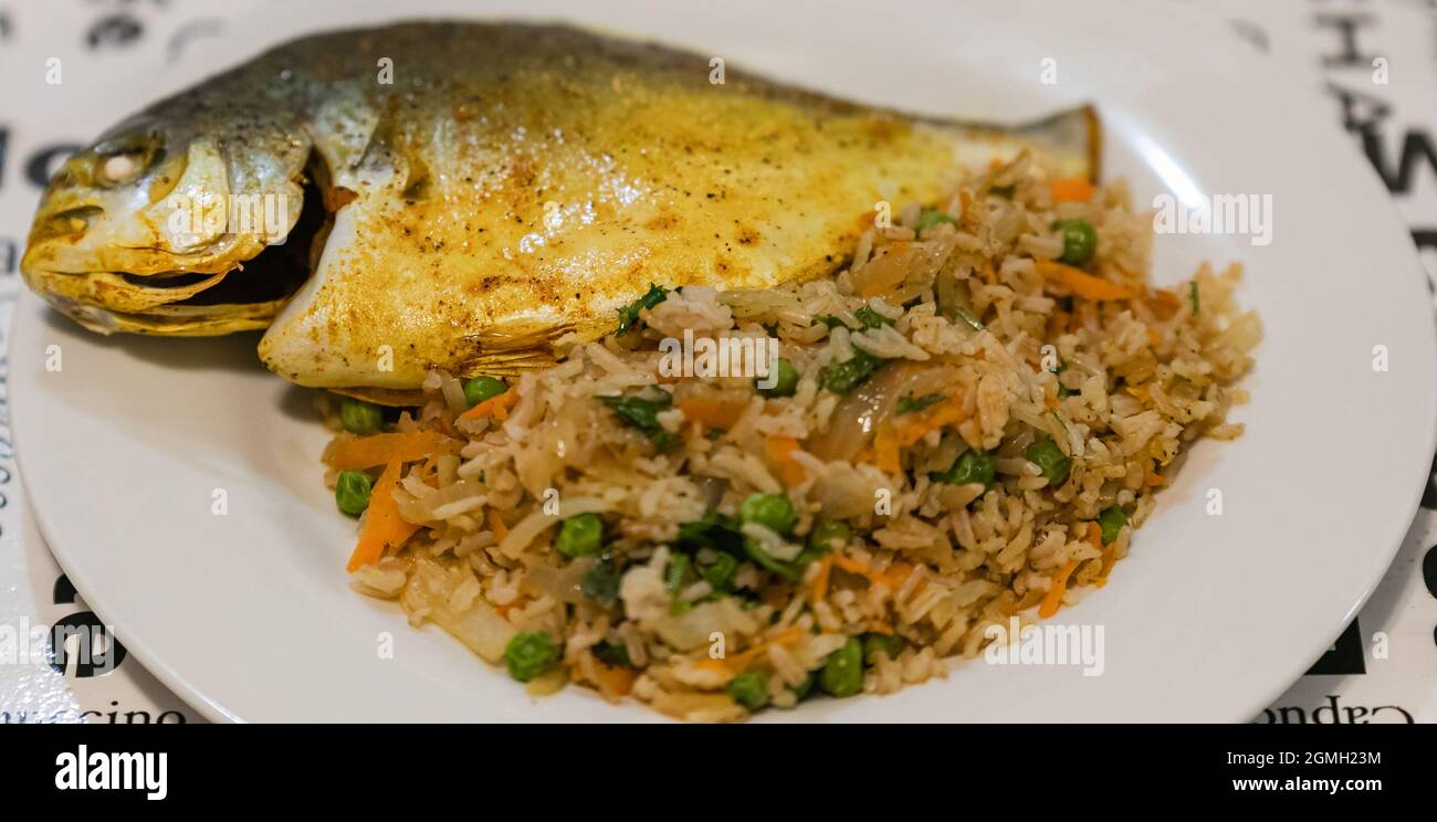 Gebratener Fisch mit Reis und Gemüse auf einem Teller. Hausmannskost Stockfoto