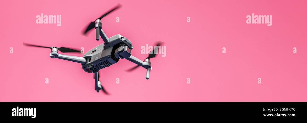 Fliegende Drohne mit Kamera auf rosa Hintergrund mit Kopierraum. Luftgetragener Quadcopter. Auch bekannt als Drohne oder UAV, unbemanntes Luftfahrzeug. Low-Angle-Vie Stockfoto