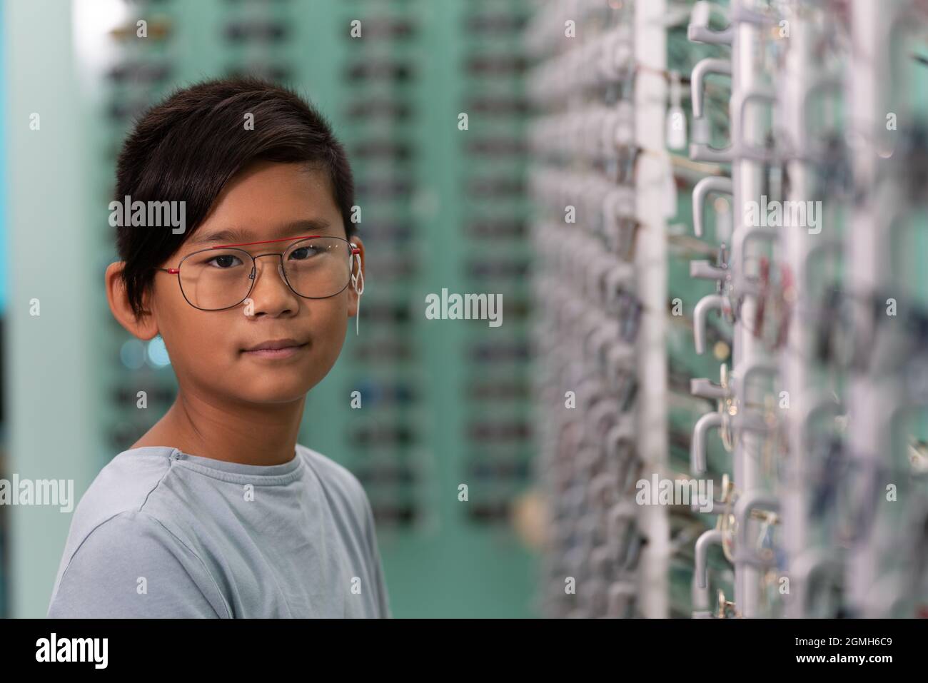 Ein asiatischer Junge, der in einem Optikerladen an einer Brille versucht. Stockfoto