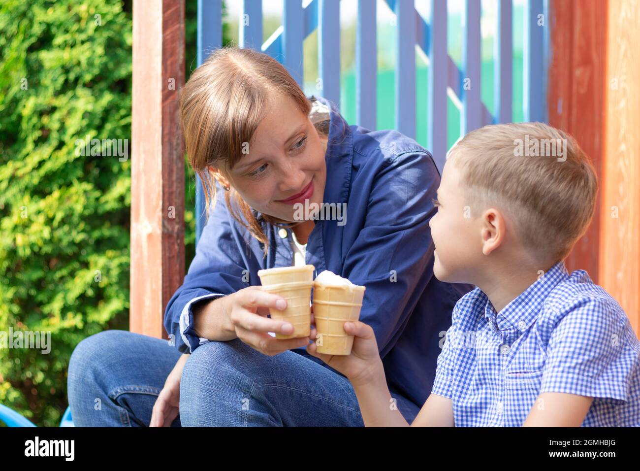 Vorschulkinder Junge mit Mama essen Eis auf der Veranda eines Hauses im Dorf an einem sonnigen Sommertag. Selektiver Fokus. Hochformat Stockfoto
