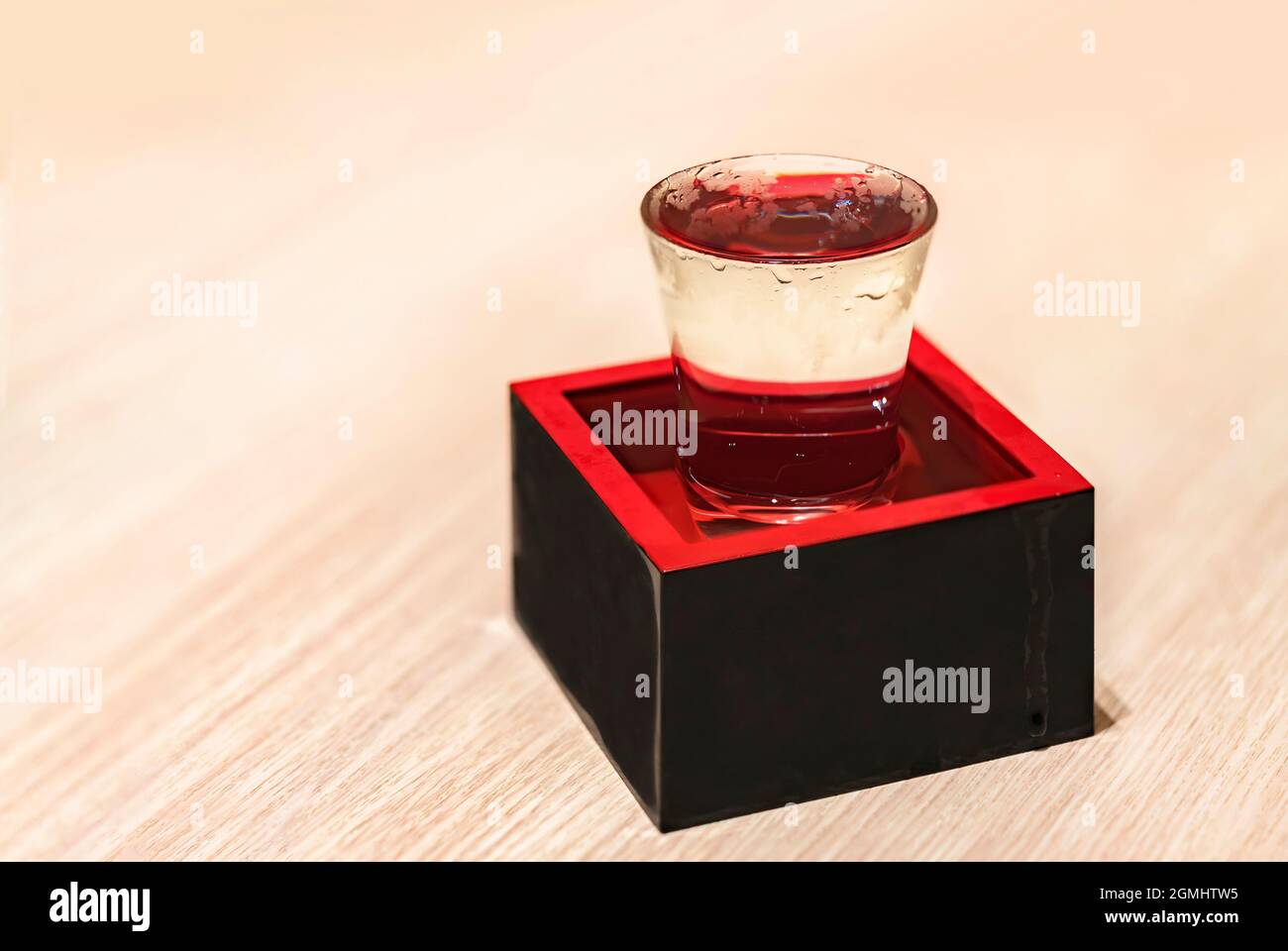 Gekühlter japanischer Reiswein namens Nihonshu in einem durchsichtigen überfließenden Sake-Serving-Schnapsglas in einer traditionellen quadratischen lackierten Holzkiste calle Stockfoto