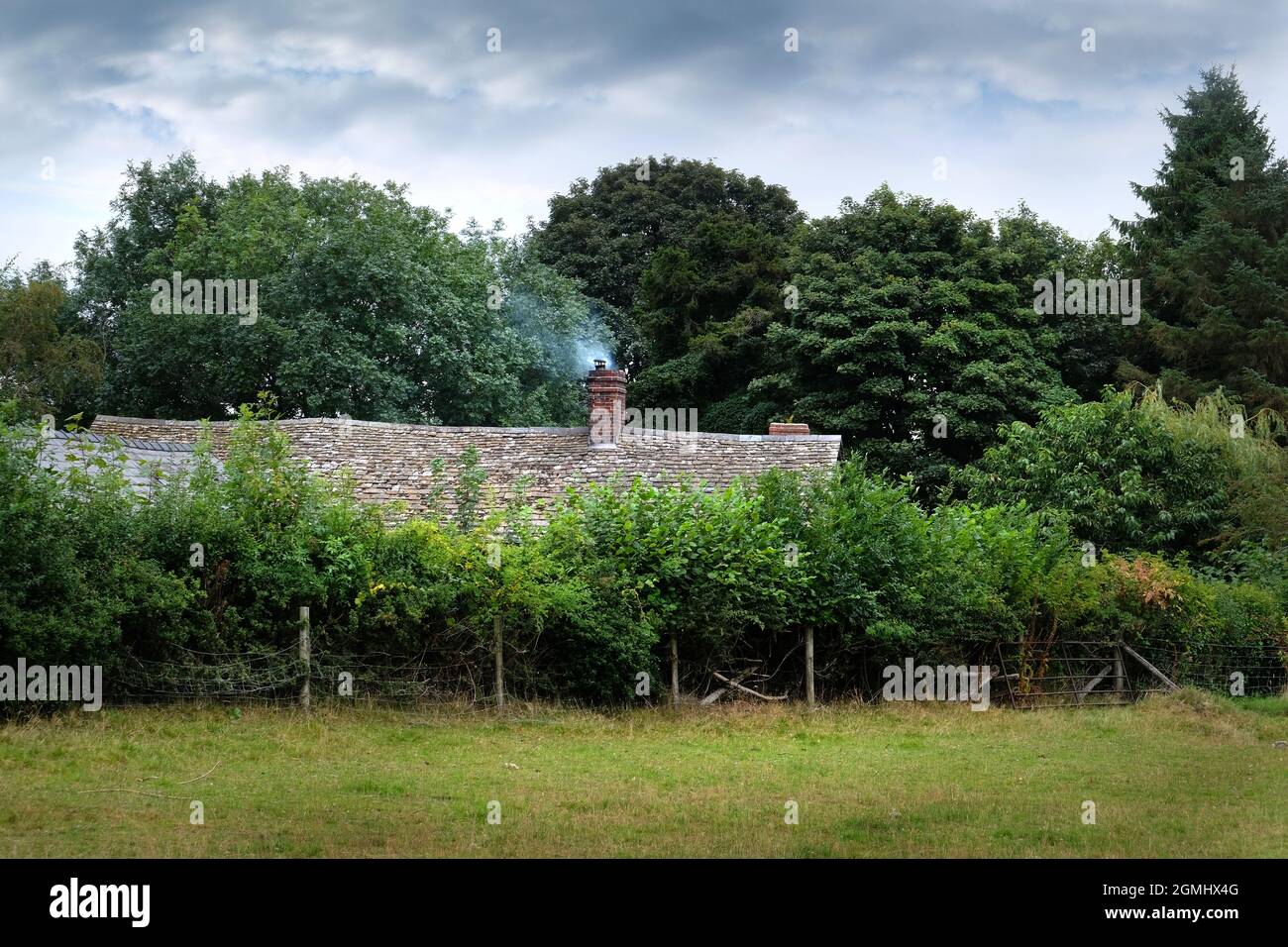 Rauchende Schornsteine eines Landhauses mit einem steingefliesten Dach in Herefordshire, England. Das Haus ist unter Bäumen versteckt Stockfoto