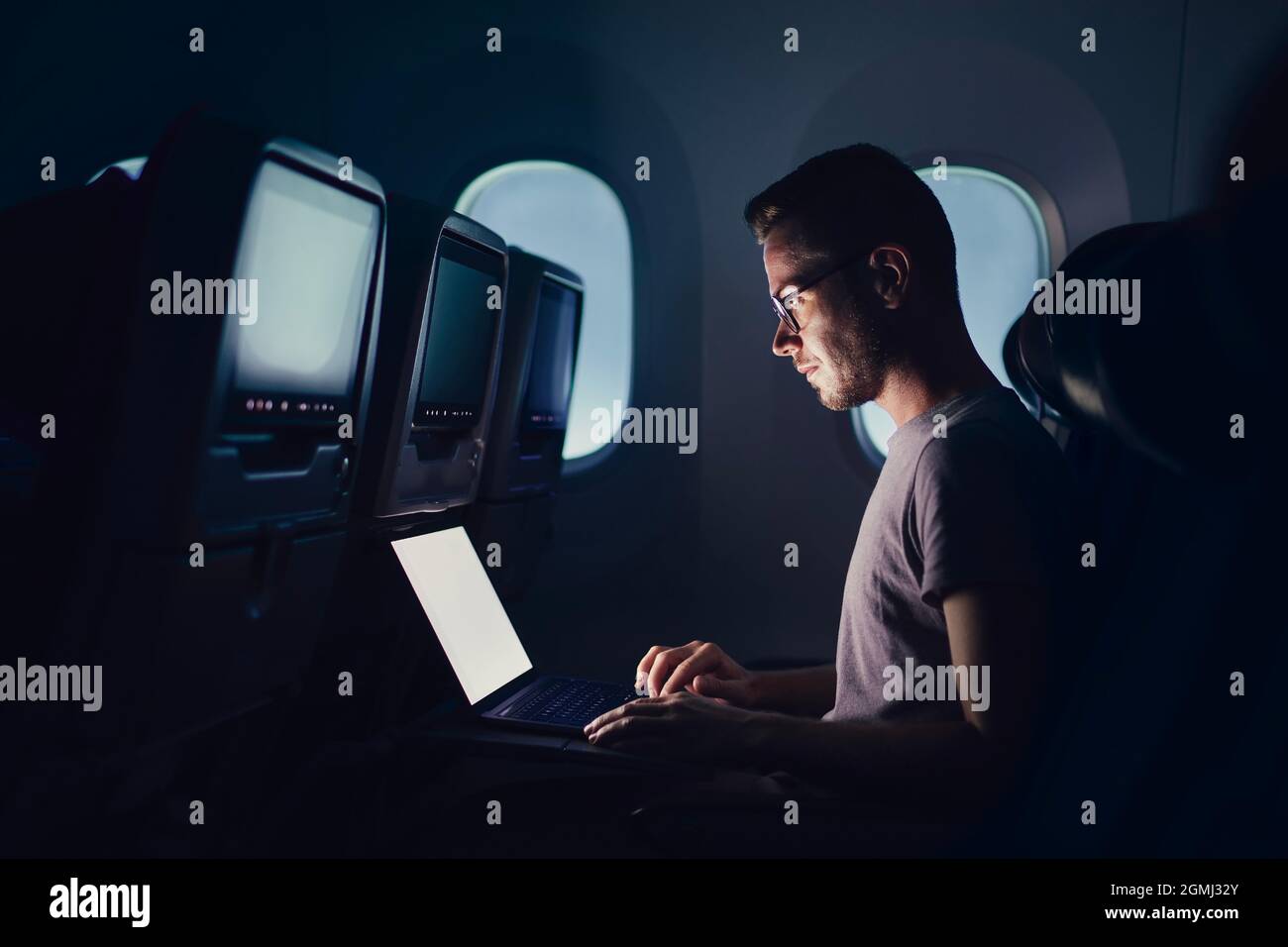 Mann, der mit dem Flugzeug reist. Junger Passagier, der während des Nachtflugs einen Laptop benutzt. Stockfoto