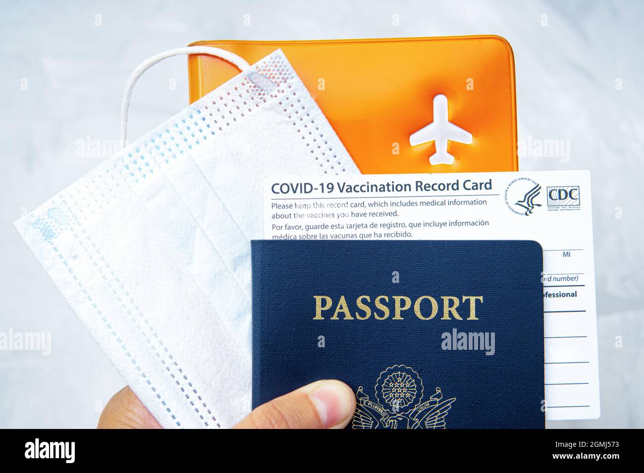US-Pass mit einer Covid-19-Impfkarte, Gesichtsmaske und Dokumenten-Organisator in der Hand. Pandemie-Zeitreisekonzept. Stockfoto