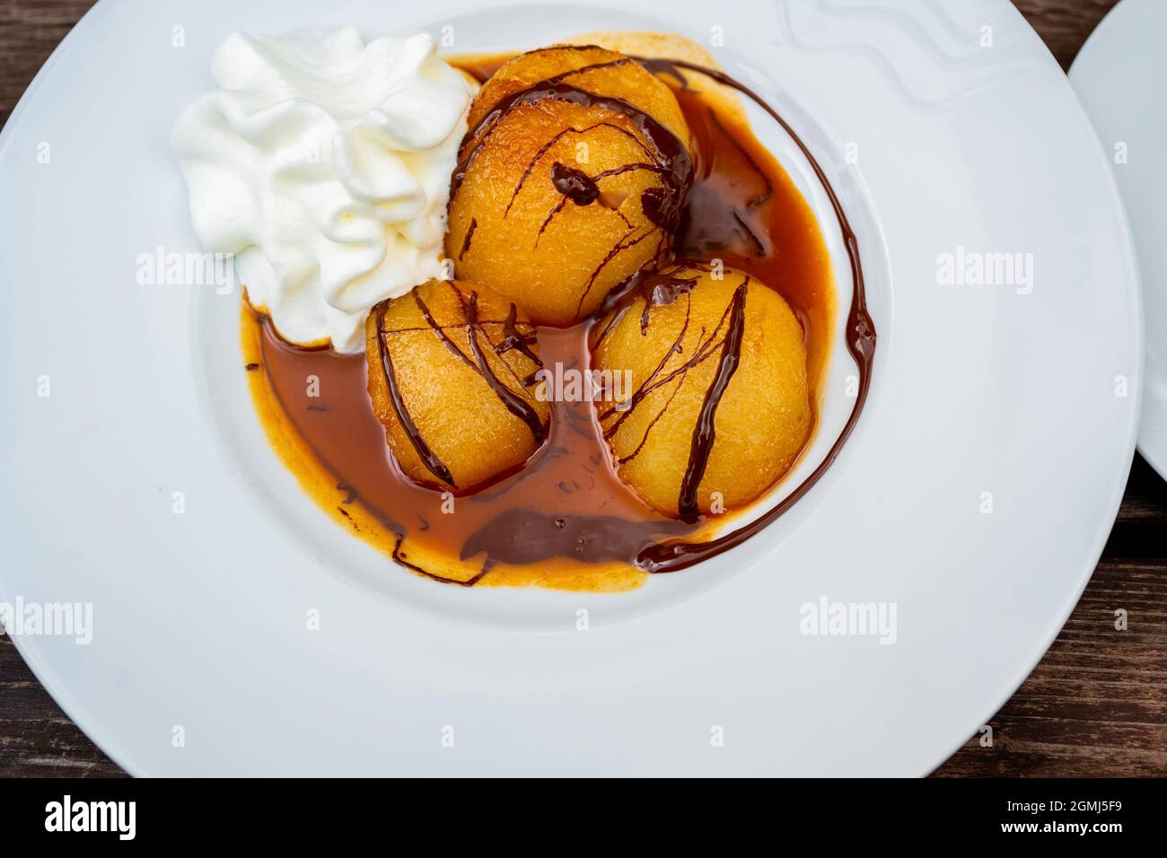 Dessert mit halbiertem Pfirsich in Karamellsauce, verziert mit Schokolade und Schlagsahne auf weißem Teller, Nahaufnahme. Stockfoto