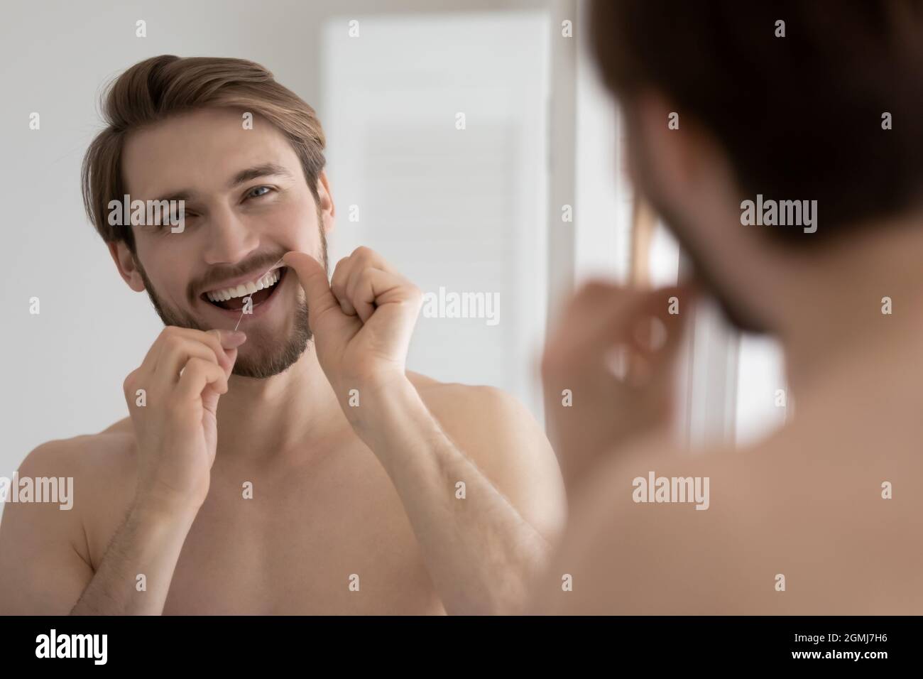Hübscher lächelnder Kerl, der Zähne mit Zahnseide putzt Stockfoto