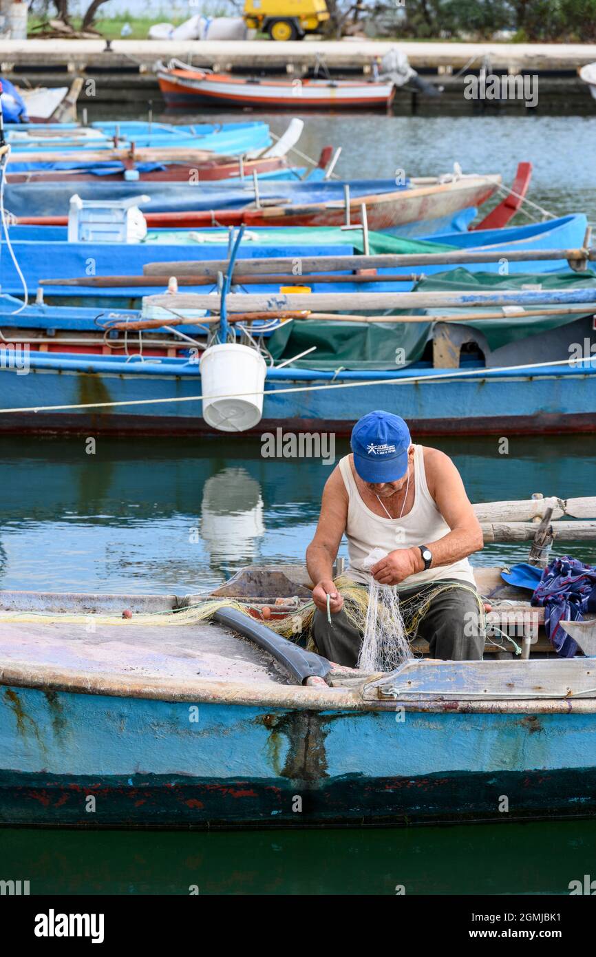 Ein Fischer, der seine Netze im Hafen im Dorf Koronisia auf der Insel Koronisia im Golf von Ambrakien, Gemeinde Arta, Epirus, Griechenland, ausbessern lässt. Stockfoto