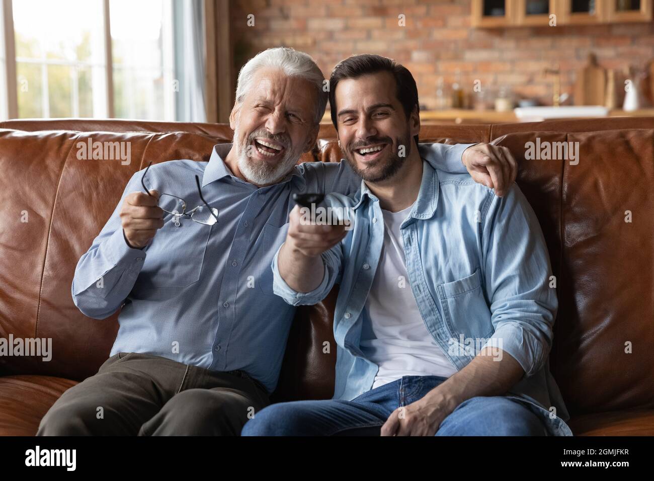Lachender junger Mann mit reiferem Vater, der zusammen Fernsehen schaut Stockfoto