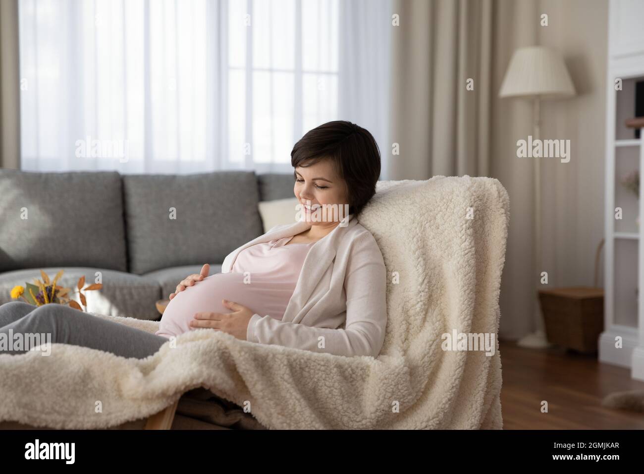 Schwangere entspannen sich im Sessel und streicheln den Bauch im Gespräch mit dem Baby Stockfoto