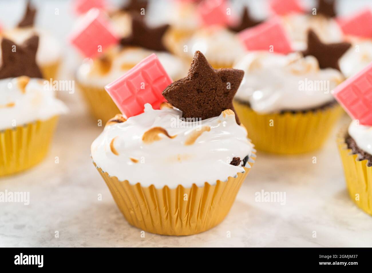 Gourmet-S'mores-Cupcakes mit Meringue-Zuckerguss und garniert mit sternförmiger Schokolade graham Cracker und einer pinken Mini-Tafel Schokolade. Stockfoto