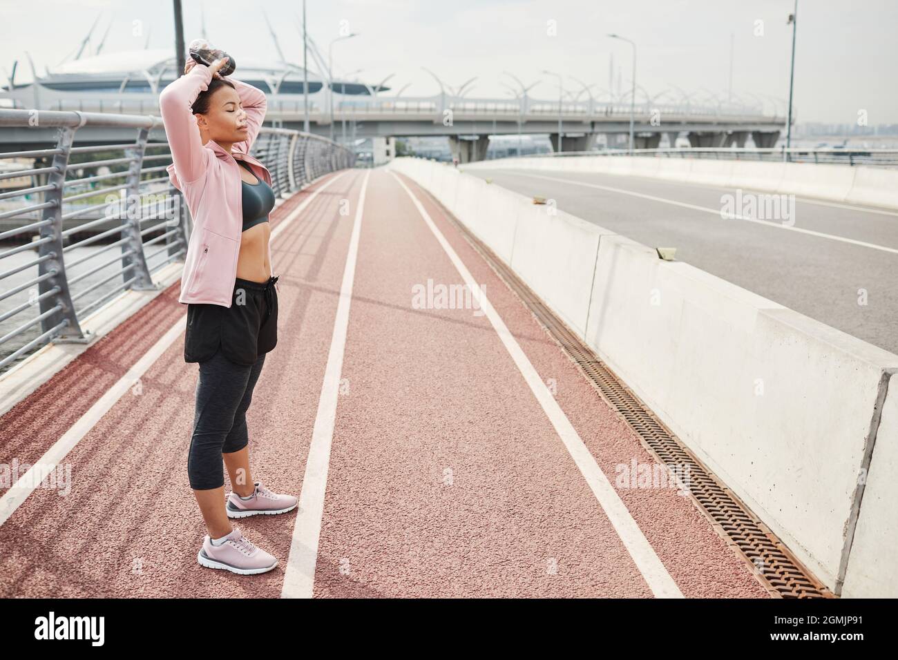 Junge Frau in Sportkleidung, die mit geschlossenen Augen steht und sich während des Sporttrainings im Freien entspannt Stockfoto