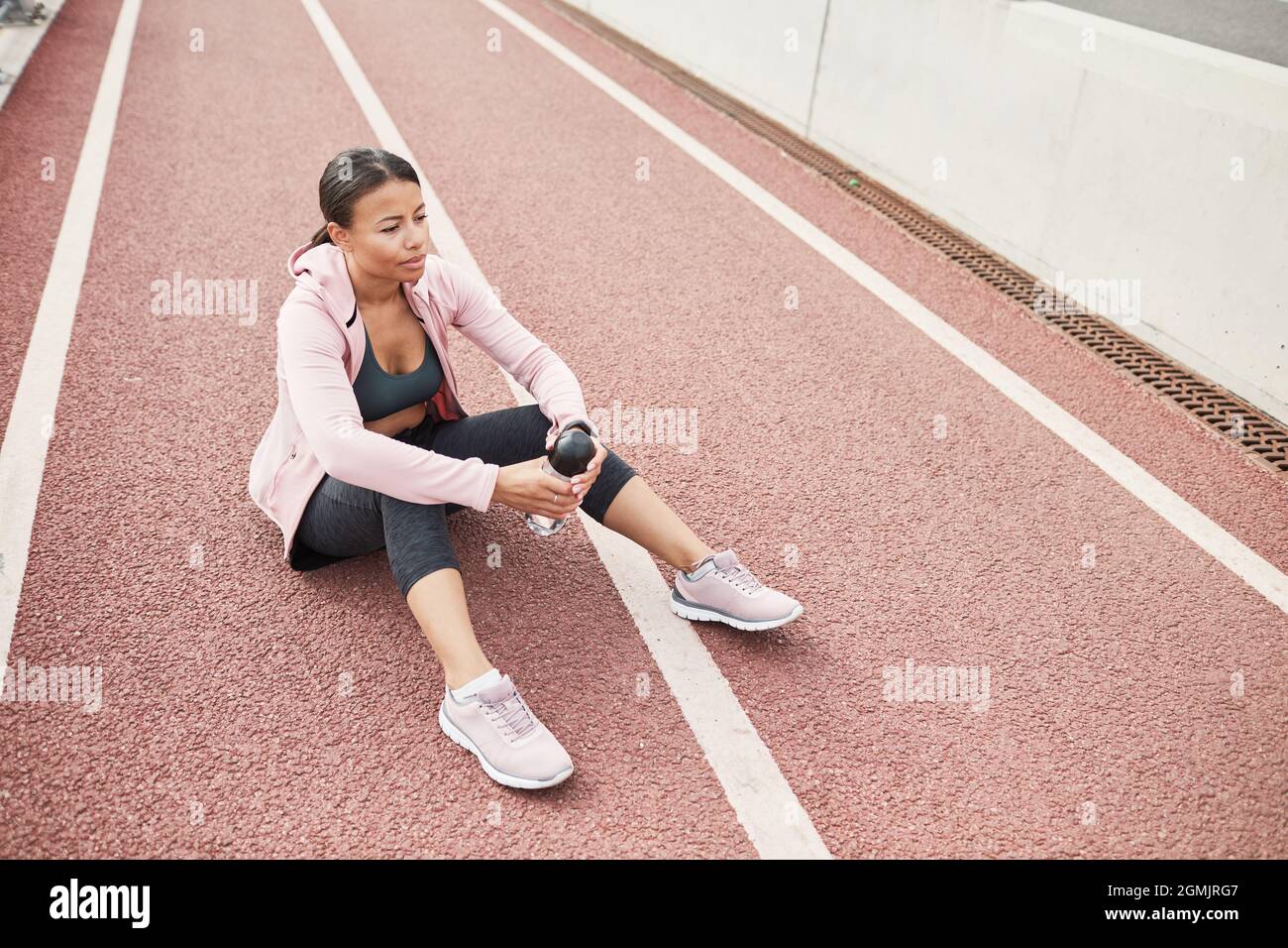Junge sportliche Frau, die mit einer Flasche Wasser auf dem Boden sitzt und sich nach dem Sporttraining im Freien ausruhte Stockfoto