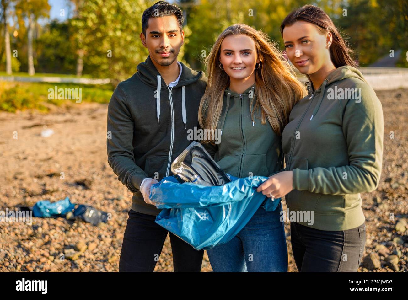 Lächelndes Team von Freiwilligen, die Müllbeutel am Strand halten Stockfoto