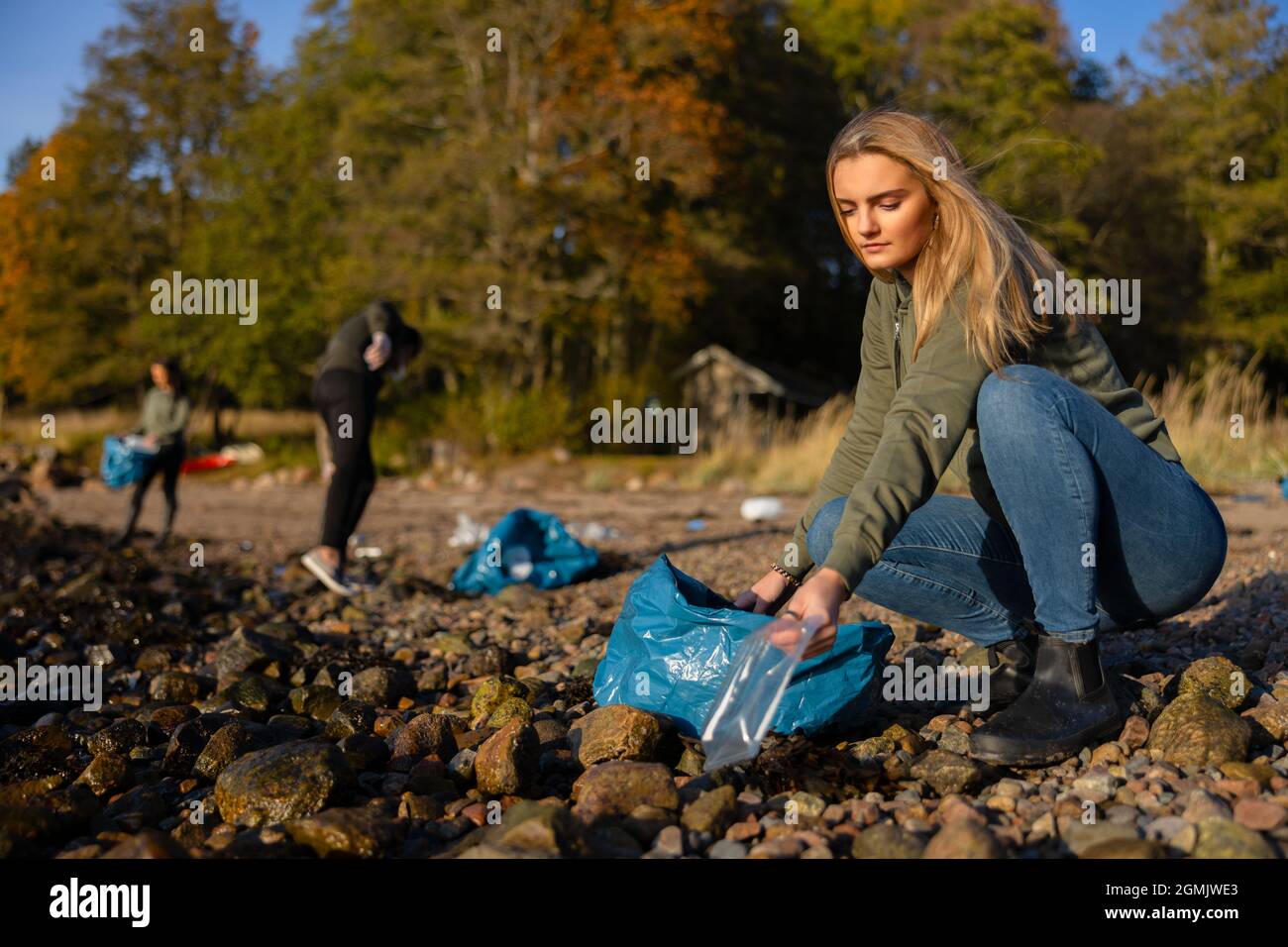 Seriöse junge Frau im Team zum Umweltschutz, die am Strand Plastik abholt Stockfoto