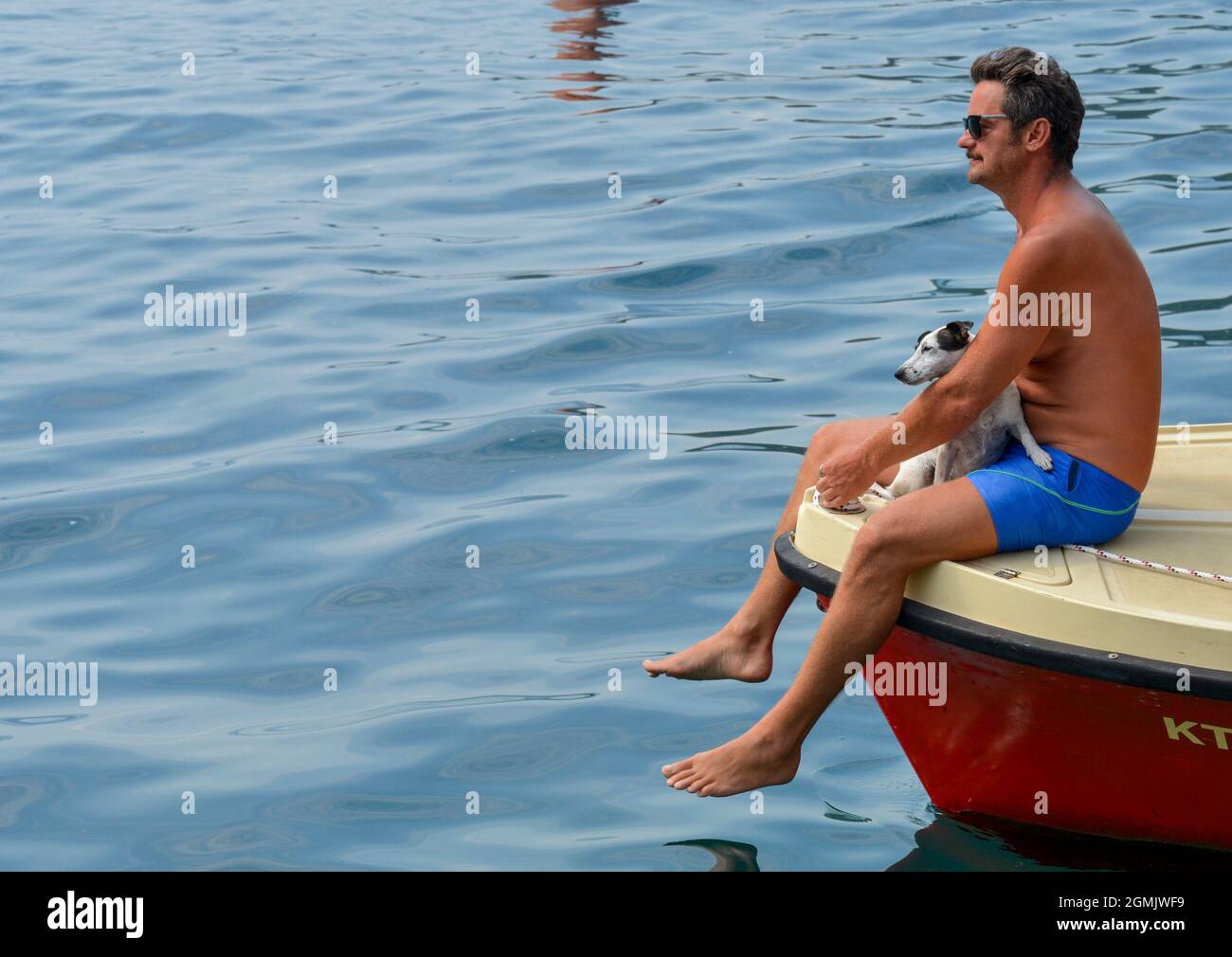 Ein Mann mit seinem kleinen Hund sitzt am Bug eines kleinen Motorbootes auf dem ruhigen Wasser der Kotor Bay. Stockfoto