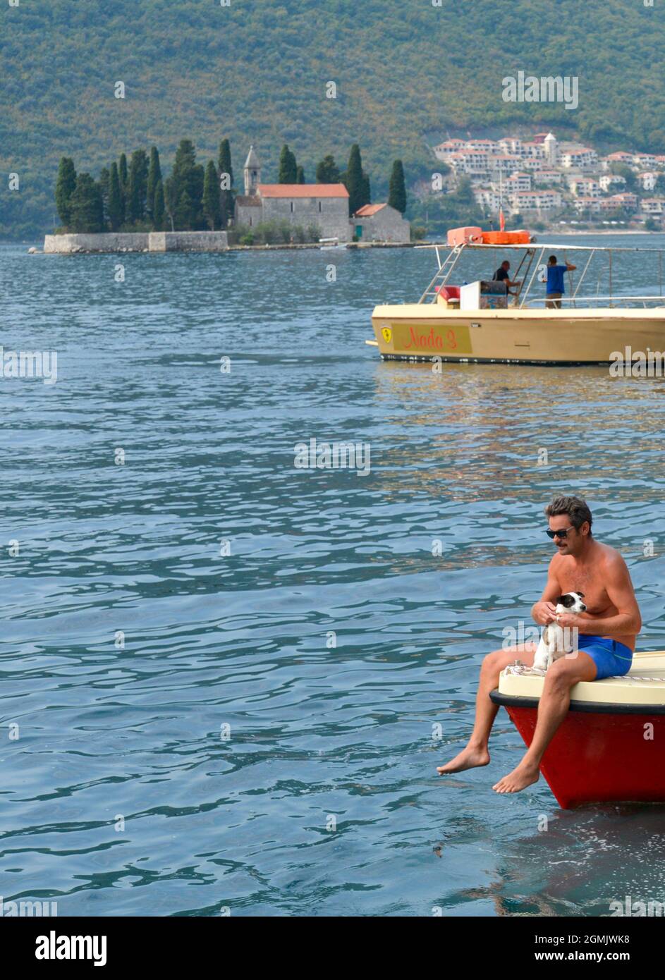Ein Mann mit seinem kleinen Hund sitzt am Bug eines kleinen Motorbootes auf dem ruhigen Wasser der Kotor Bay. Stockfoto