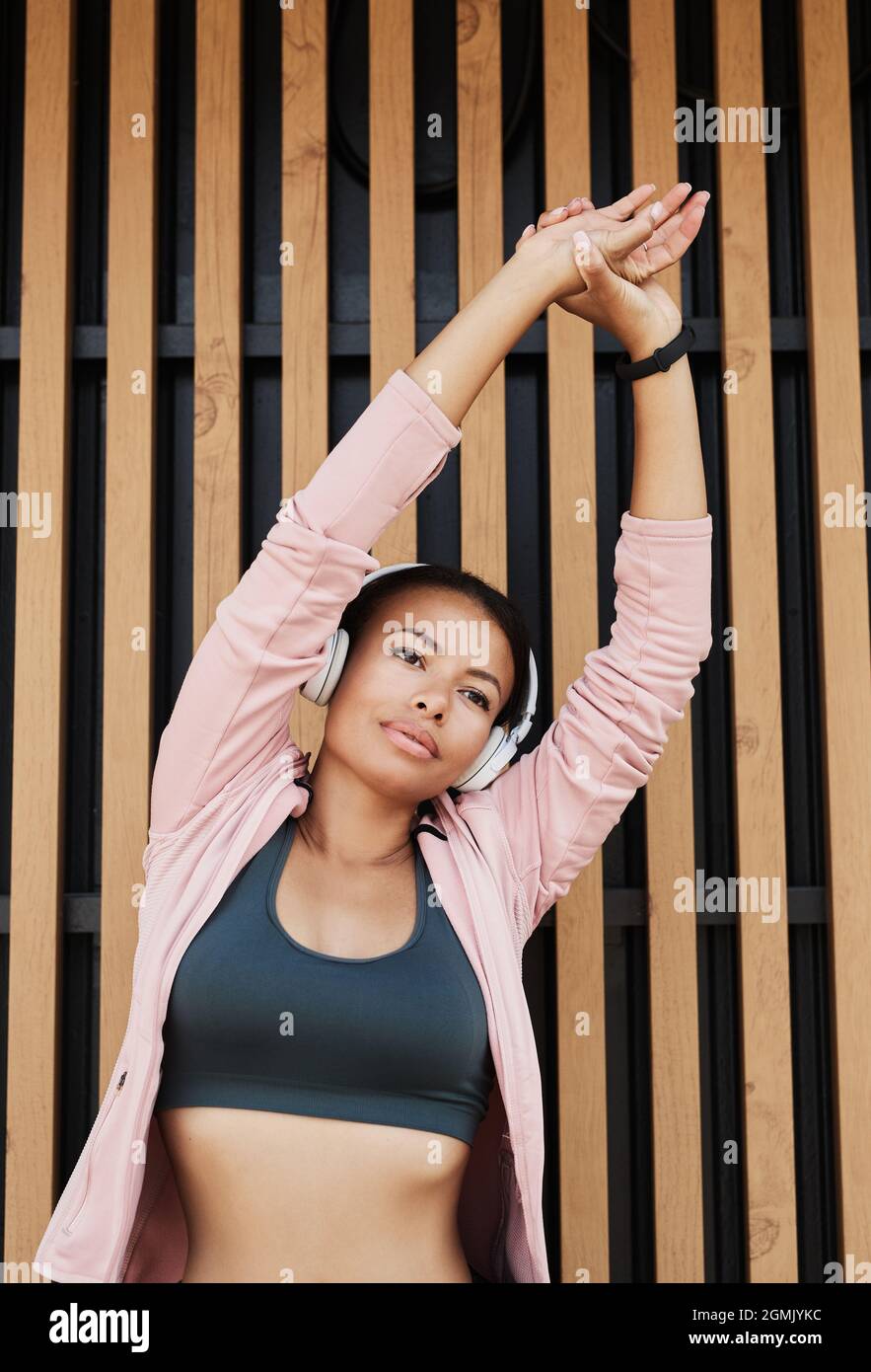 Afrikanische junge Frau hört Musik in kabellosen Kopfhörern, hebt ihre Arme und trainiert während des Trainings im Freien Stockfoto