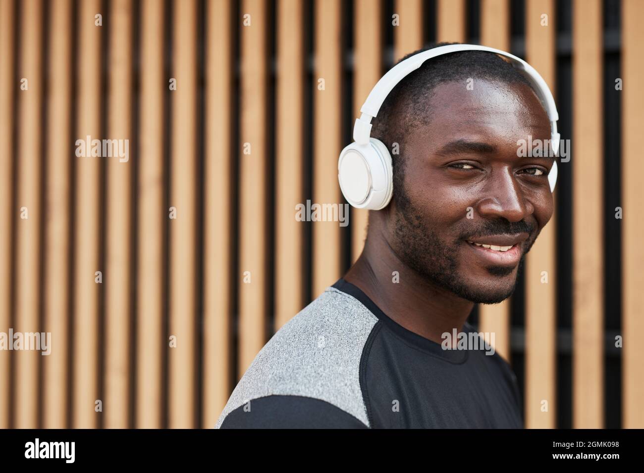 Porträt eines afrikanischen jungen Mannes in kabellosen Kopfhörern, der beim Spaziergang durch die Stadt die Kamera anlächelt Stockfoto