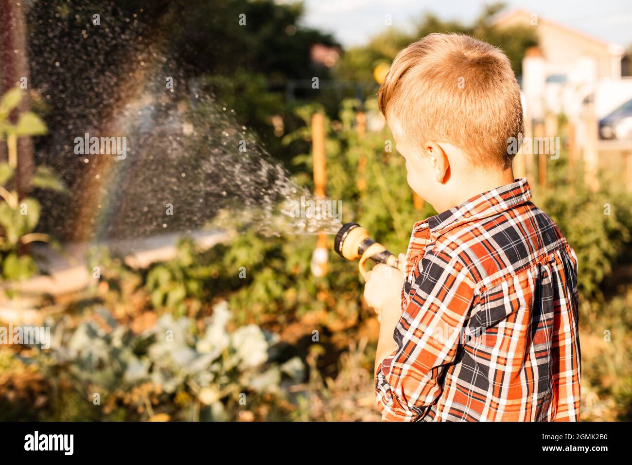 Der Junge genießt einen Regenbogen, während er im Garten wässert Stockfoto
