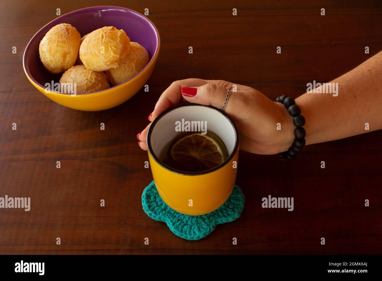 Eine weibliche Hand, die einen Becher Tee und eine Schüssel mit Käsebuns hält. Stockfoto