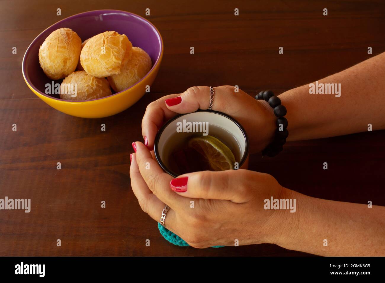 Weibliche Hände halten einen Becher Tee und eine Schüssel Käsebuns auf der Seite. Stockfoto