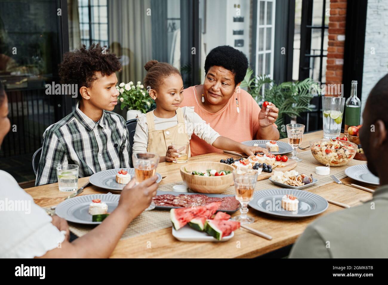 Porträt einer großen afroamerikanischen Familie, die gemeinsam im Freien zu Abend essen und fröhlich lächeln Stockfoto