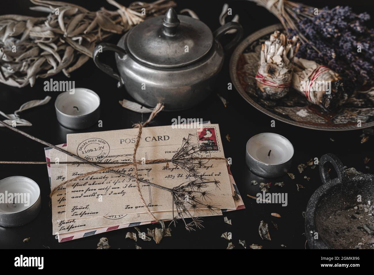 Altes, Vintage aussehendes Paket von Postkarten, handgeschrieben in Kursivschrift auf einem dunkelschwarzen unordentlichen Tisch. Getrocknete Wildblumen auf einem Brief. Stockfoto