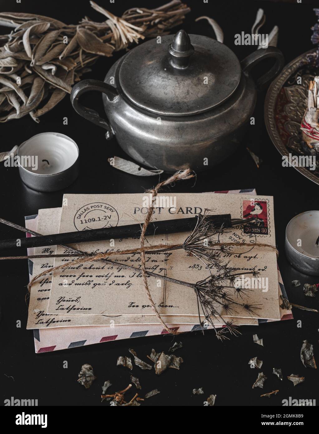 Altes, Vintage aussehendes Paket von Postkarten, handgeschrieben in Kursivschrift auf einem dunkelschwarzen unordentlichen Tisch. Getrocknete Wildblumen auf einem Brief. Vertikal Stockfoto