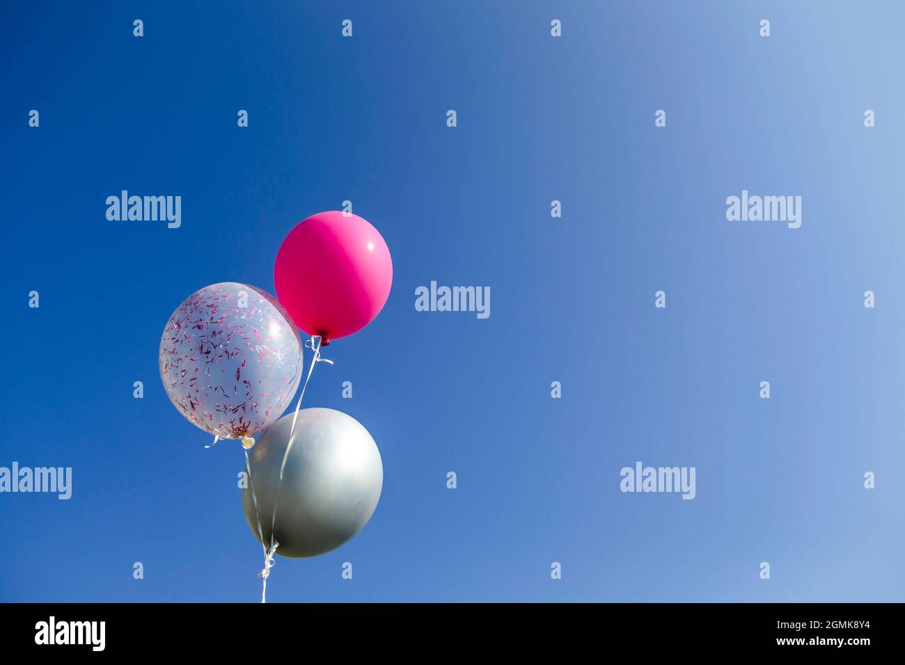 Drei farbenfrohe Heliumballons zum Geburtstag, die am Himmel schweben. Für Ihren Text verfügbarer Speicherplatz kopieren. Stockfoto