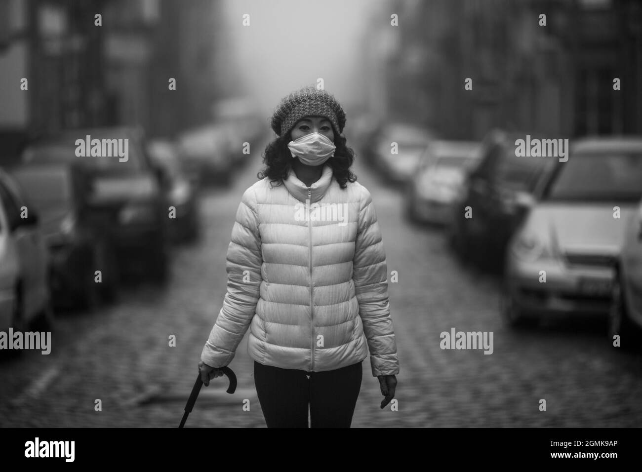 Eine Frau in antiviraler Maske steht bei bewölktem Wetter auf der Straße. Schwarzweiß-Foto. Stockfoto