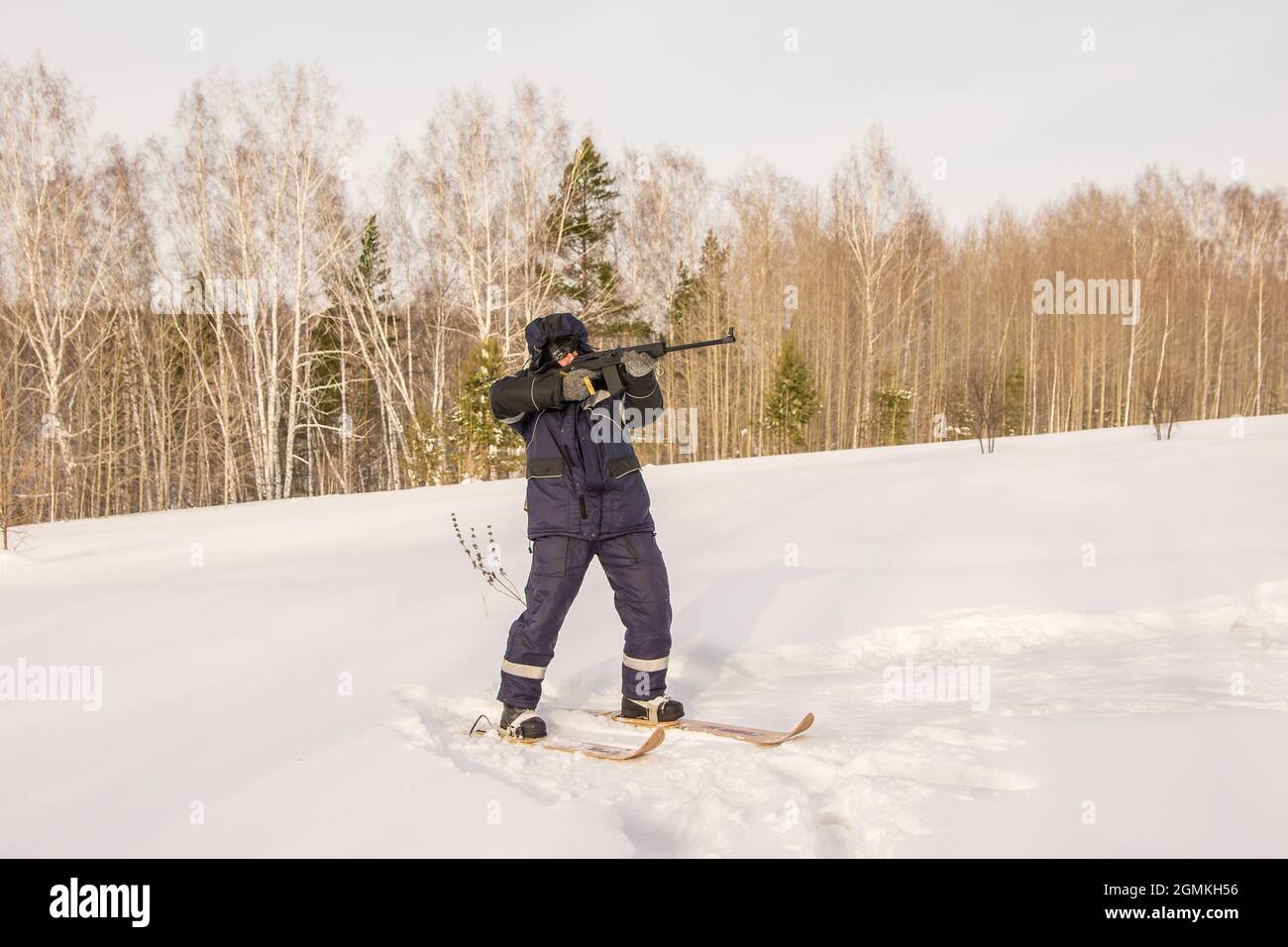 Ein Jäger oder Wilderer steht auf Skiern am Waldrand und zielt mit einer automatischen Waffe auf Beute oder Ziel Stockfoto