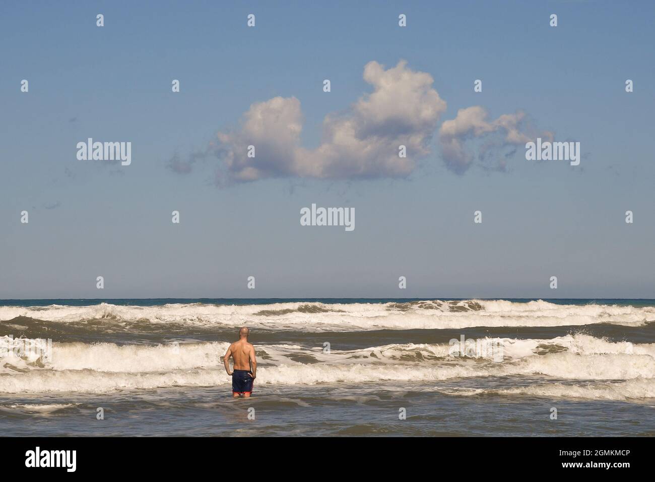 Rückansicht eines Mannes, der an einem windigen Sommertag an der Küste mit hohen weißen Wellen steht, Marina di Castagneto Carducci, Livorno, Toskana, Italien Stockfoto