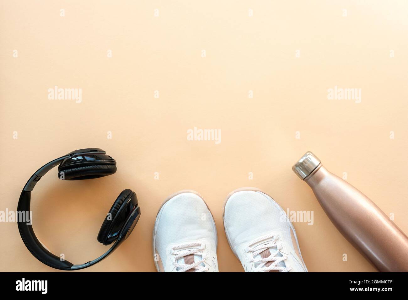 Weiße Sneaker, Kopfhörer und Flasche mit Wasser auf pastellorangefarbenem Hintergrund. Konzept für gesundes Leben, Sport und Training. Flach liegend, Draufsicht, Kopie Stockfoto