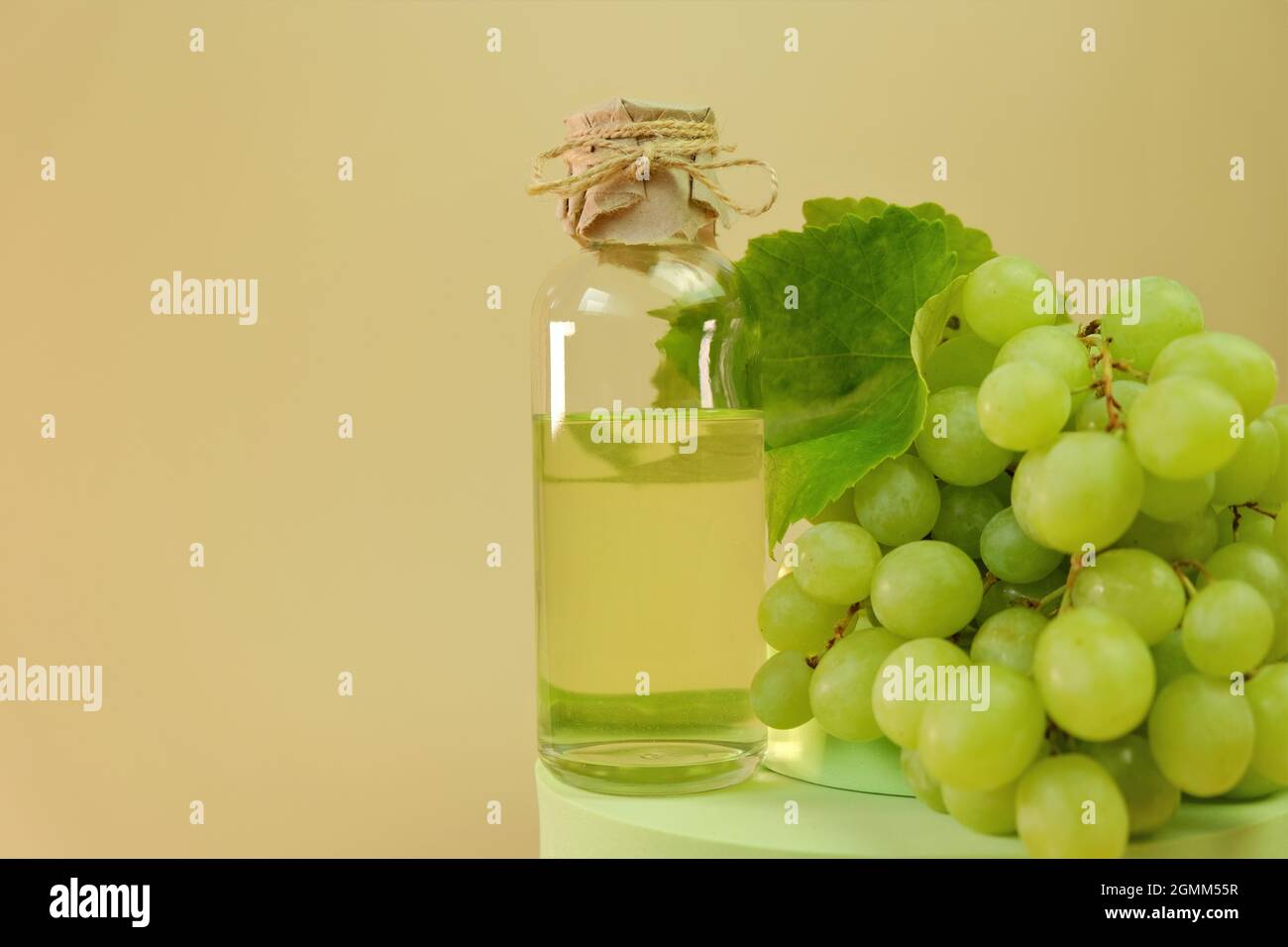 Traubenkernöl.Flasche und Bund grüner Trauben auf beigem Hintergrund. Bio Natürliches Traubenkernöl. Stockfoto