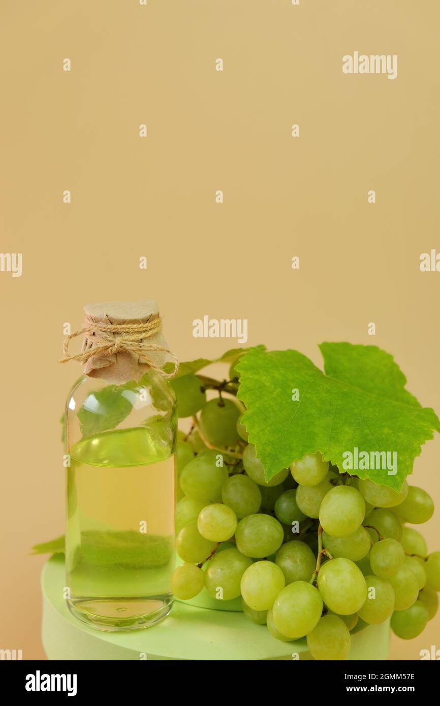 Traubenkernöl.Flasche und Bund grüner Trauben auf dem Podium auf beigem Hintergrund. Natürliches Bio-Traubenkernöl. Stockfoto