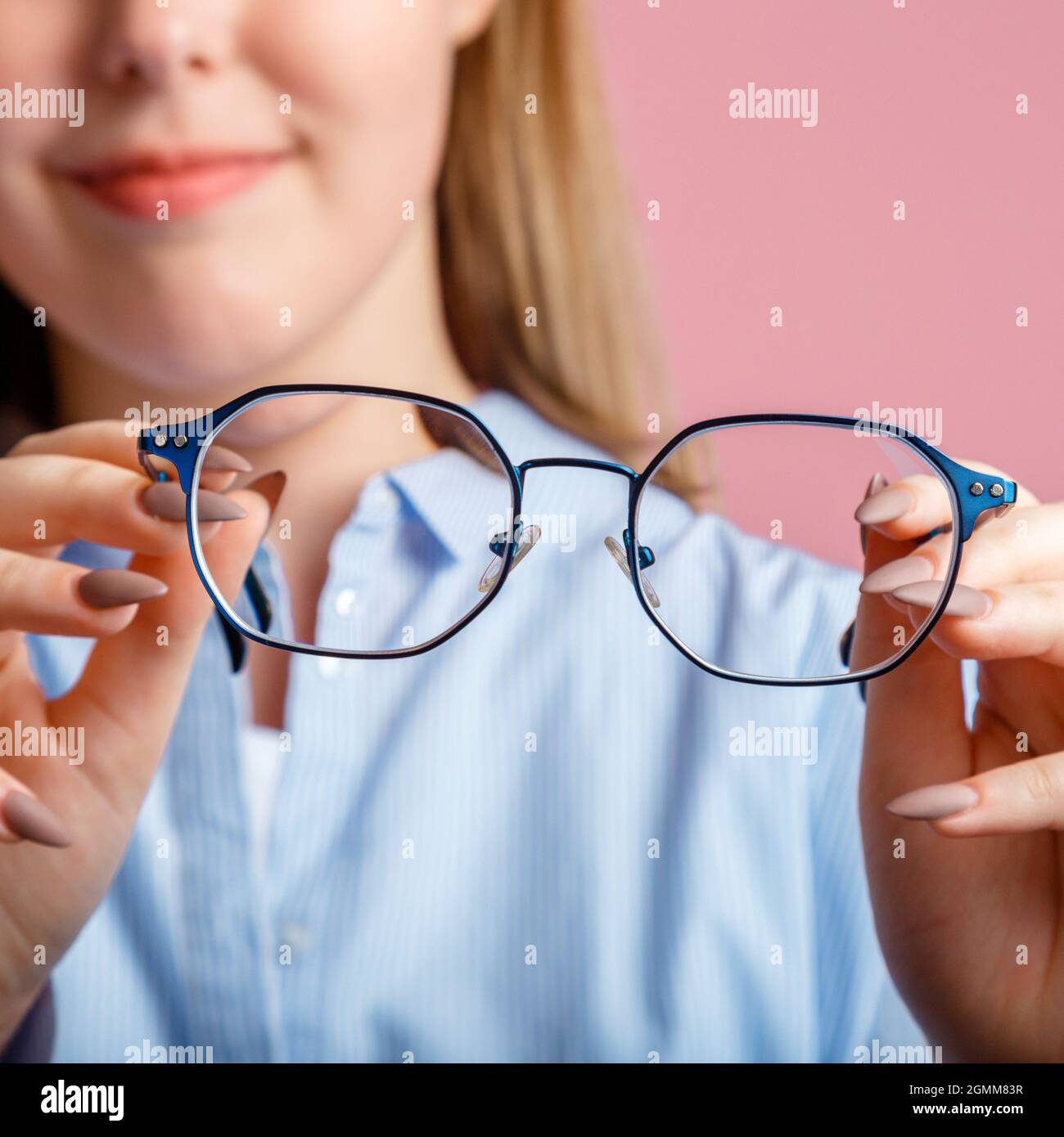 Brillen in den Händen. Blaue modische Metallgläser für das Sehen in den Händen lächelnder junger Frau. Augengesundheitsprüfung, Sehkorrektur über Brillen Stockfoto