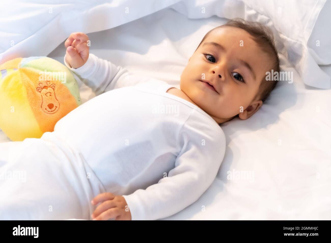 Ich wachte gerade auf entzückendes 5 Monate altes kaukasisches Baby lächelnd in einem grauen T-Shirt und einem Ball zum Spielen Stockfoto