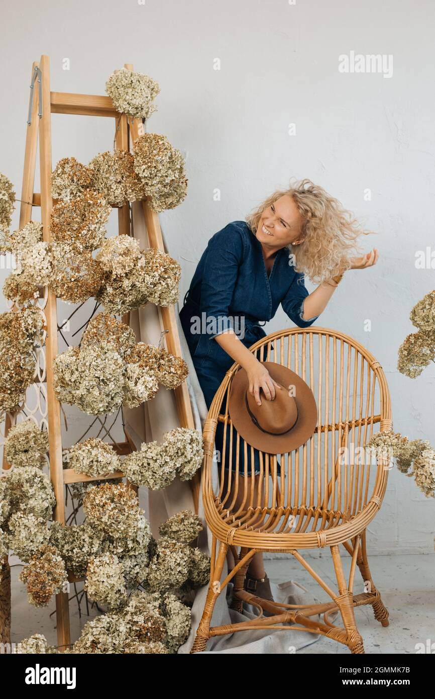 Frau Floristin in Denim blauen Kleid ist glücklich. Schöne Blumenarrangement einschließlich schöner getrockneter Hortensien Blumen, in stilvollem Raum, auf Holz Stai Stockfoto