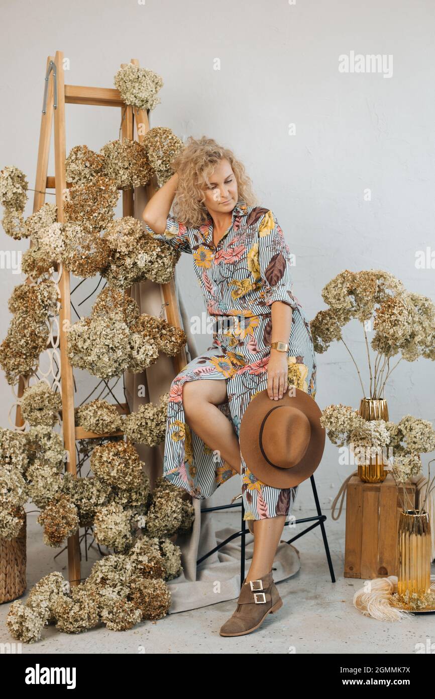 Eine Frau Floristin in Kleid schaut aus und träumt. Schöne Blumenarrangement einschließlich schönen getrockneten Hortensien Blumen, in stilvollem Raum, auf Holz s Stockfoto