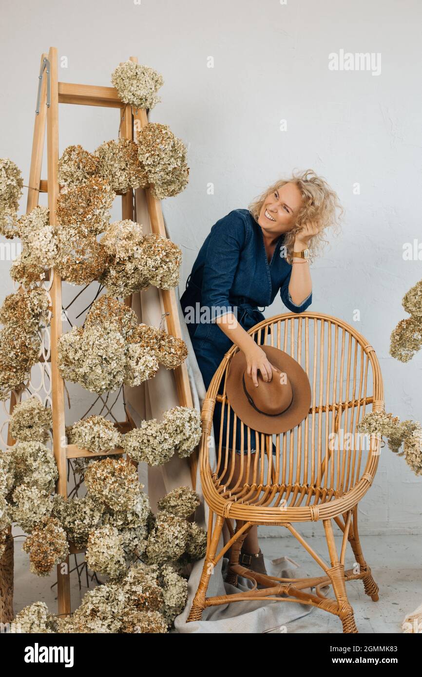 Schöne Blumenarrangements mit schönen getrockneten Hortensien Blumen, in stilvollem Raum, auf Holztreppe. Unter ihnen ist eine fröhliche lächelnde Frau flori Stockfoto