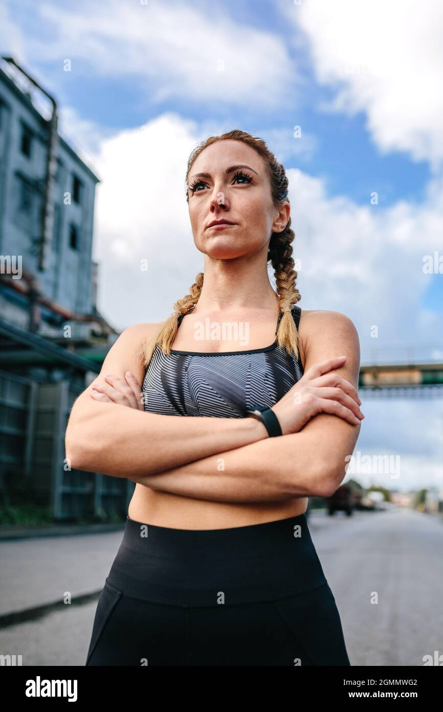 Sportliche Frau mit gekreuzten Armen, die vor einer Fabrik posiert Stockfoto