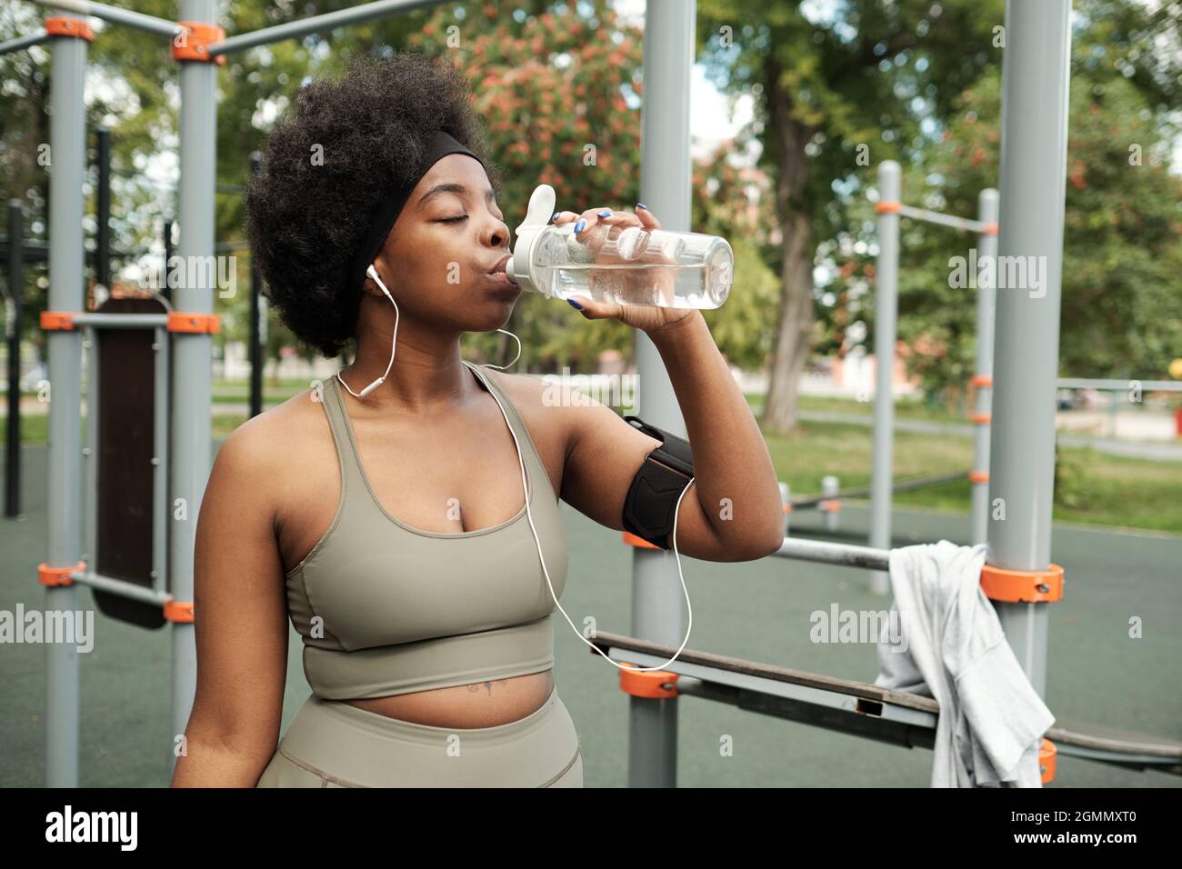 Durstige Sportlerin im Trainingsanzug mit Wasser, bevor sie das Sporttraining fortsetzt Stockfoto
