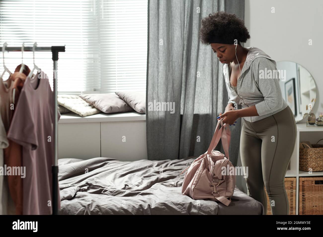 Junge Sportlerin in Activewear, die ihre Handtasche auf das Bett legt, während sie sich für das Training im Freien vorbereitet Stockfoto