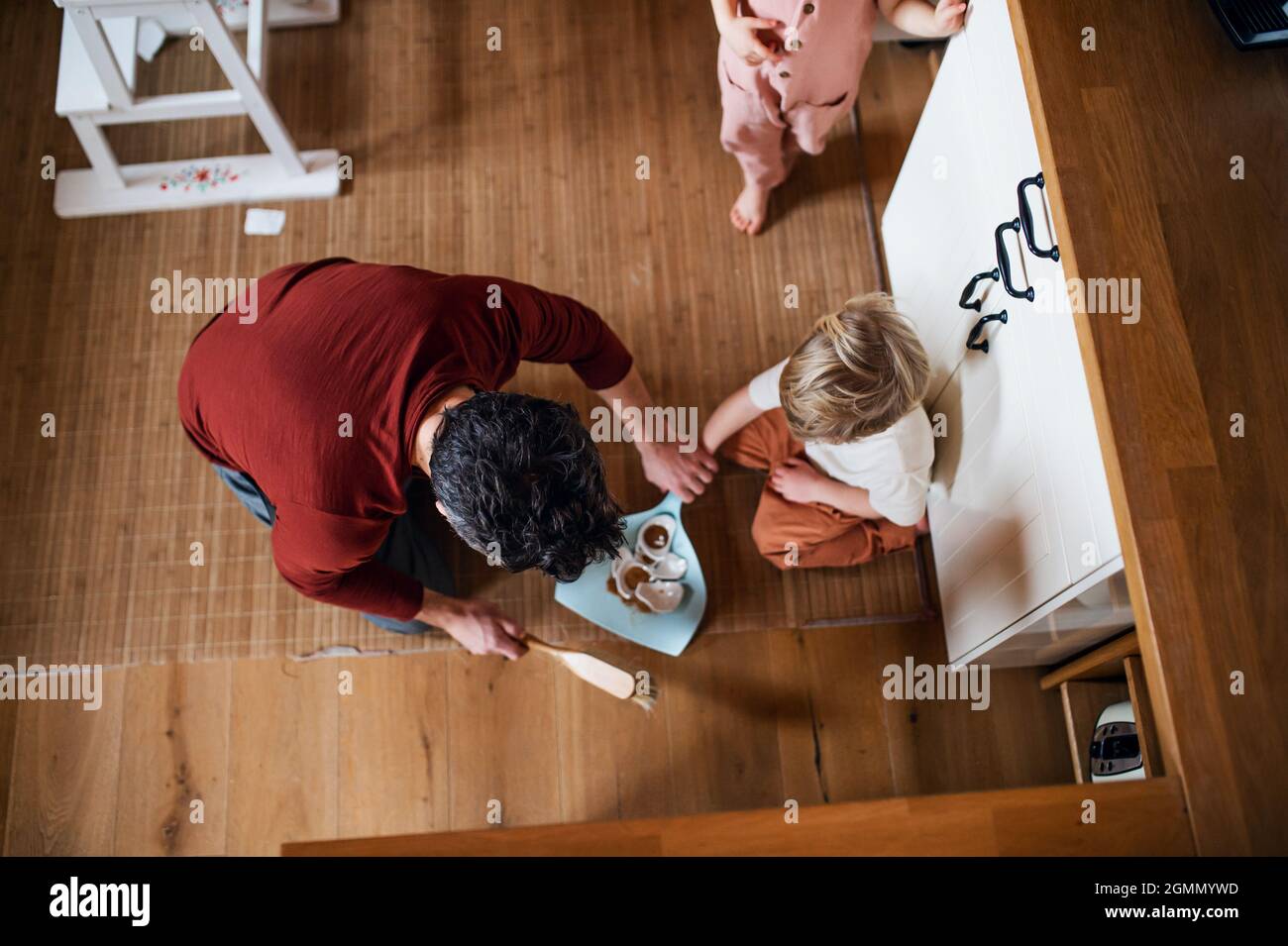 Draufsicht auf Vater mit kleinen Kindern fegenden Scherben zu Hause, tägliche Hausarbeit Konzept. Stockfoto