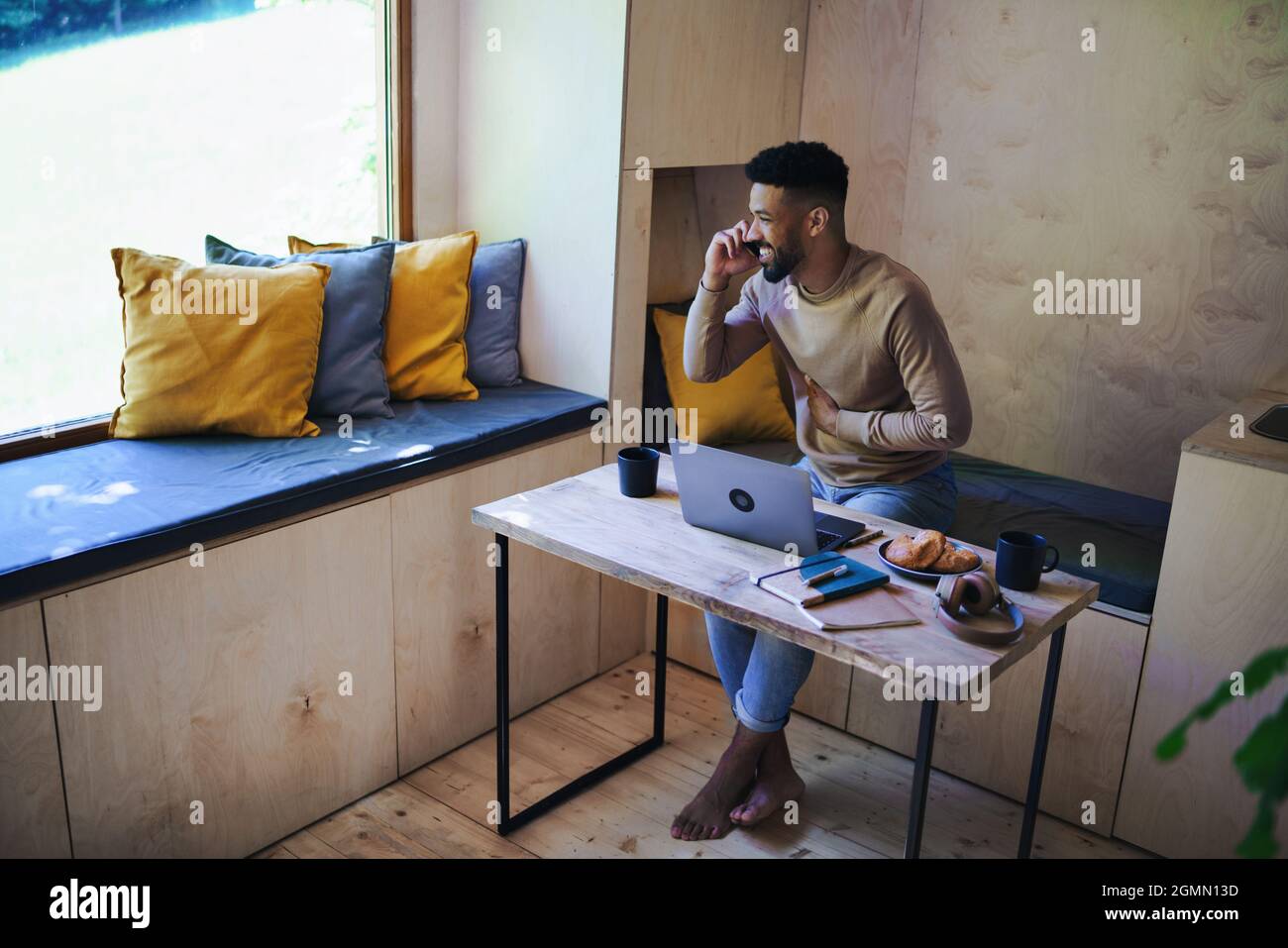 Glücklicher junger Mann mit Laptop und Smartphone, der drinnen in einem Baumhaus sitzt, Wochenendausflug und Remote-Office-Konzept. Stockfoto
