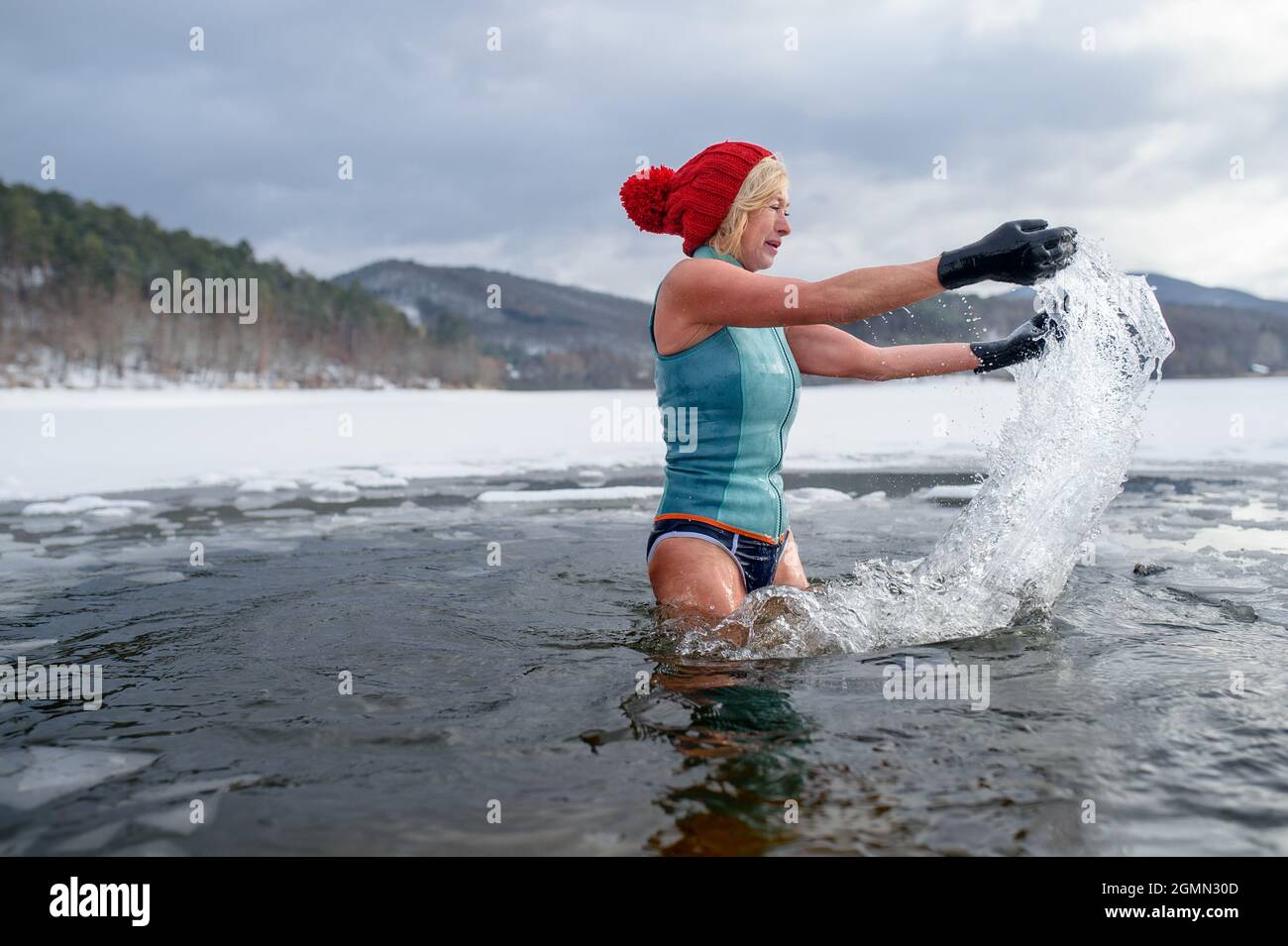 Aktive ältere Frau im Badeanzug im Winter im gefrorenen See, Kalttherapie-Konzept. Stockfoto